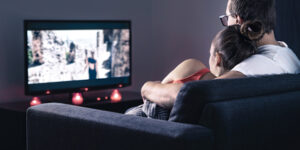 肩を寄せ合ってテレビを見ている女性と男性の写真